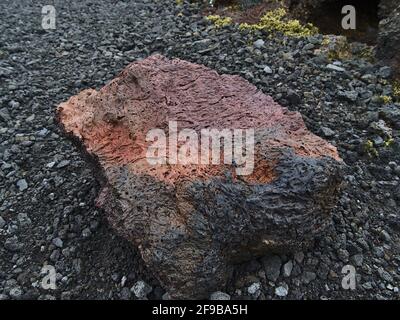 Nahaufnahme eines porösen, farbenfrohen Vulkangesteins mit roten, orangen und schwarzen Farben auf einem Wanderweg neben einem Lavafeld in der Nähe von Gridavik, Reykjanes, Island. Stockfoto