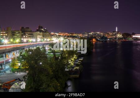 Blick auf die Skyline von Washington DC mit einem erhöhten Highway, der nachts am Ufer des Potomac-Flusses verläuft. Leichte Wanderwege. Stockfoto