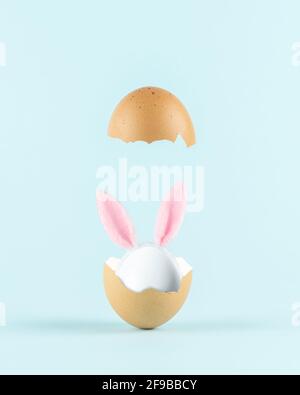 Weißes Ei mit Kaninchenohren in gebrochener Eierschale auf pastellblauem Hintergrund. Minimales Osterkonzept. Kreatives Happy Easter oder Frühlingslayout. Stockfoto