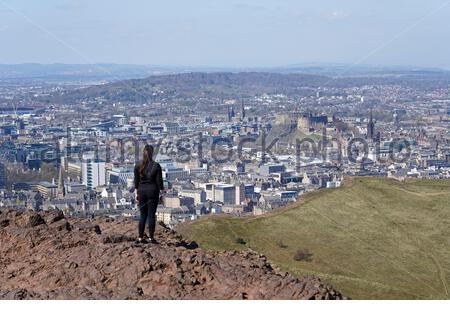 Edinburgh, Schottland, Großbritannien. April 2021. Am ersten vollen Wochenende, an dem Reisebeschränkungen in ganz Schottland aufgehoben wurden, strömen die Menschen zu den üblichen Besucherherden, um die Sonne und die Natur im Holyrood Park zu genießen. Blick über die Dächer der Stadt auf das Edinburgh Castle vom Gipfel des Arthur's Seat. Kredit: Craig Brown/Alamy Live Nachrichten Stockfoto