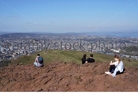 Edinburgh, Schottland, Großbritannien. April 2021. Am ersten vollen Wochenende, an dem Reisebeschränkungen in ganz Schottland aufgehoben wurden, strömen die Menschen zu den üblichen Besucherherden, um die Sonne und die Natur im Holyrood Park zu genießen. Blick über die Dächer der Stadt auf das Edinburgh Castle vom Gipfel des Arthur's Seat. Kredit: Craig Brown/Alamy Live Nachrichten Stockfoto