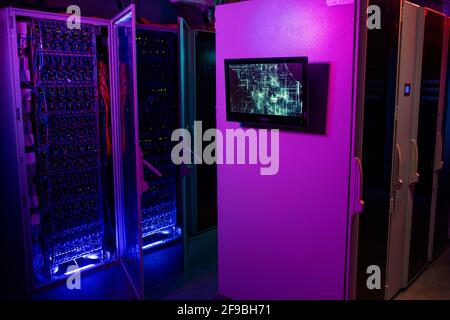 Monitor am Server-Rack-Schrank im Rechenzentrum in neonvioletten und blauen Farben, offener Schrank mit blauen Kabeln im Hintergrund Stockfoto