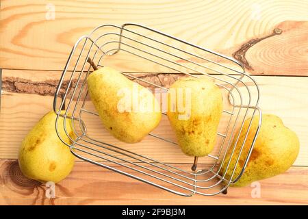 Vier hellgelbe organische, reife, saftige, süße Birnen in einem Weidenkorb aus einem Draht, Korb, Nahaufnahme, auf einem Holztisch. Stockfoto