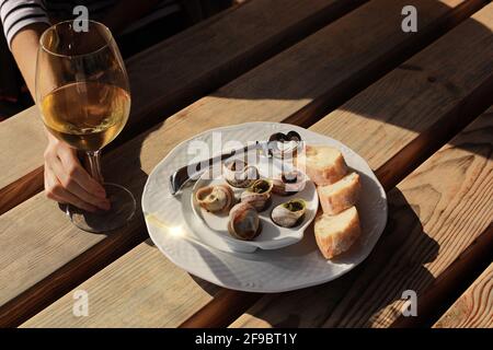 Mädchen, die im Café im Freien sitzt und die Schnecken mit Kräutern, Butter und Weißwein genießt. Stockfoto