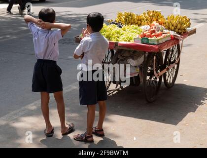 Zwei Schuljungen, die in der Nähe eines Obstverkaufskorbs stehen und im Vorort Dadar in Mumbai, Maharashtra, Indien, Asien, auf den Verkäufer warten. Stockfoto