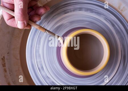 Nahaufnahme der männlichen Hand, die einen Pinsel hält und mit einem Töpferrad auf eine Keramik malt. Draufsicht Stockfoto