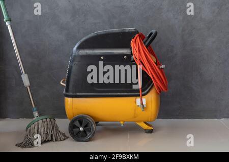 Die elektrischen Luftpumpen mit Wischmopp werden auf einem grauen Fliesenboden hinter unbemalten Gipswänden platziert. Stockfoto