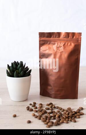 Leere Kaffeeverpackung auf einem Holztisch, mit Kaffeesamen, mit dekorativer Blume auf weißem Hintergrund, Kaffeeverpackung Mockup mit leerem Raum zu Stockfoto
