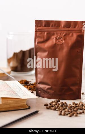 Leere Kaffeeverpackung mit Kaffeesamen, Buch und Glas mit gemahlenem Kaffee, Kaffeeverpackung Mockup mit leerem Raum, um Ihr Branding des zu zeigen Stockfoto