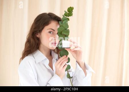 Junge Frau hält Glas von Creme und Zweig von Pflanzenhaut Auge. Eukalyptus in Öko-Kosmetik Stockfoto