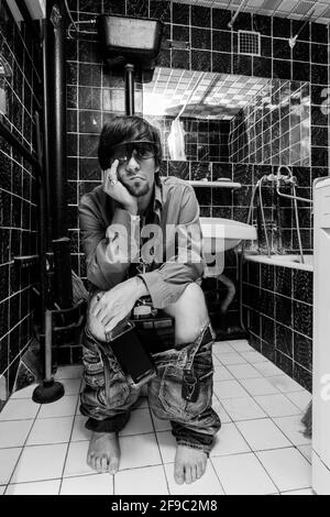 Betrunkener Mann sitzt in einer Toilette mit einer Alkoholflasche Stockfoto