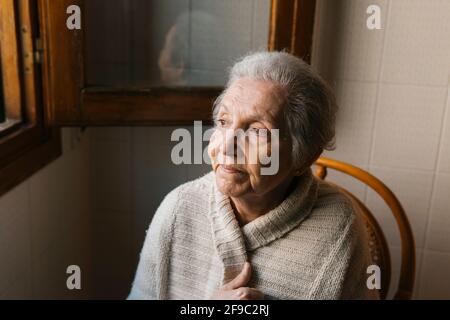 Porträt einer älteren Frau, die aus dem Fenster schaut Stockfoto