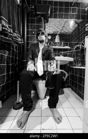 Betrunkener Mann sitzt in einer Toilette mit einer Flasche Whiskey Stockfoto