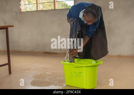 Dodoma, Tansania. 08-18-2019. Ein schwarzes Mädchen putzt in einer Grundschule in einem ländlichen Gebiet in Tansania den Boden ihres Klassenzimmers mit Seife Stockfoto