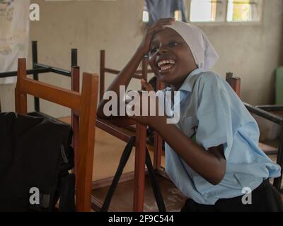 Dodoma, Tansania. 08-18-2019. Porträt eines muslimischen Mädchens, das nach dem Schultag in ihrem Klassenzimmer lächelt und sich darauf vorbereitet, die Schule zu verlassen Stockfoto