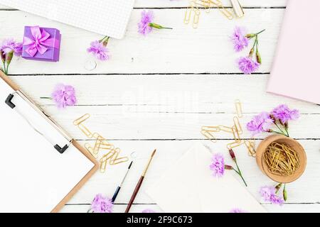 Arbeitsbereich mit Klemmbrett, Notizbuch, Blumen und Accessoires. Weiblicher Blog-Arbeitsbereich. Flach liegend, Draufsicht. Stockfoto