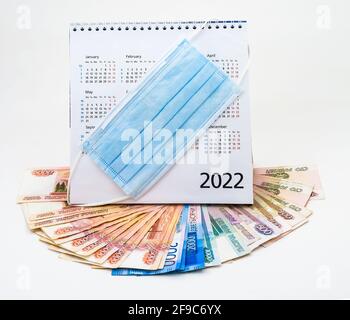 Kalender 2022 und Papierrubel. Medizinische Maske und Kalender 2022. Die Maske auf dem Kalender und das russische Geld. Stockfoto