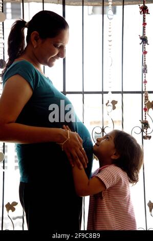 Mumbai; Maharashtra; Indien - März. 11; 2011 - schöne Tochter berührt den schwangeren Bauch der Mutter. Glückliches kleines Mädchen Gefühl Baby bei Mutter Bauch und awa Stockfoto