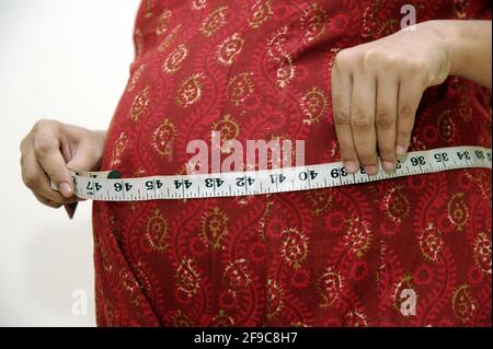Mumbai; Maharashtra; Indien; Asien; April. 11; 2011 - Junge schwangerische inderin, die ihren Bauch isoliert auf weißem Hintergrund misst Stockfoto