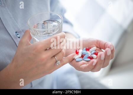 Genug Pillen für eine Überdosis eine Person, die in der Hand einer Frau mit einem Glas Wasser in der anderen Hand gehalten wird. Stockfoto