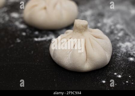 Drei rohe georgische Khinkali, die mit Mehl auf einem schwarzen Tisch bestreut wurden. Seitenansicht Stockfoto