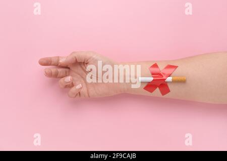 Eine Zigarette, die mit einem Kreuz an die Hand einer Frau geklebt wurde, gab das Rauchen auf. Stockfoto