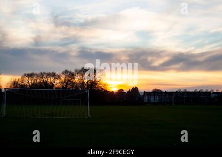 Sonnenuntergang auf dem örtlichen Fußballplatz mit den Toren im Vordergrund und Bäumen, Häusern im Hintergrund. Bild bei schwachem Licht mit Sonnenuntergang und CO Stockfoto