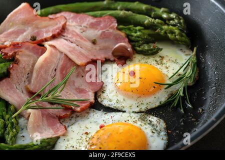 Gebratener Spargel mit Speck, Eiern und Gewürzen in einer Pfanne in Nahaufnahme Stockfoto