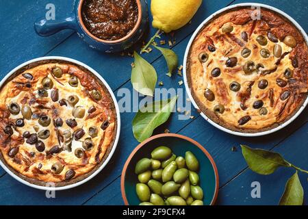 Hausgemachte Tarte mit Oliven auf altem blauem Holzhintergrund, dekoriert mit frischer Zitrone, frischen Oliven, Zitronenblättern und Feigenmarmelade von oben Stockfoto