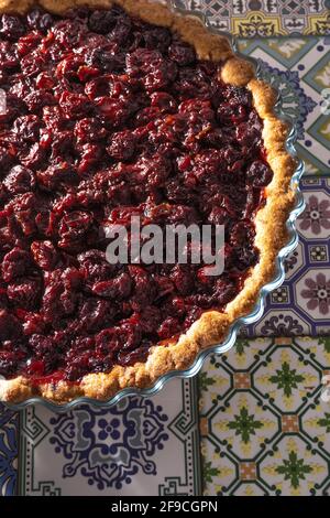 Cherry Pie, Blick von oben. Hausgemachtes Backen. Runde, offene Tarte mit Füllung. Gießen von Gebäck auf dem Tisch der farbigen Fliesen Stockfoto