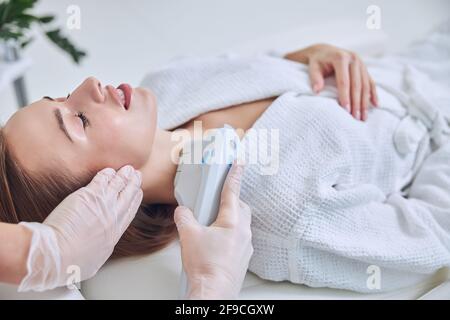 Charmante elegante kaukasische rothaarige Frau genießen tolle Zeit im Spa Salon, während die Hautpflege auf modernen Gerät im Spa Salon Stockfoto