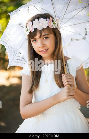 Schöne kaukasische Mädchen für die Kommunion im Park mit gekleidet Ein Regenschirm, der die Kamera anschaut Stockfoto