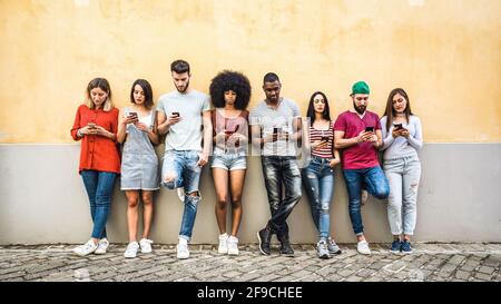 Multirassische Freunde, die im Garten der Uni ein Smartphone gegen die Wand benutzen - Junge Menschen süchtig nach Handy - Technologie Konzept Stockfoto