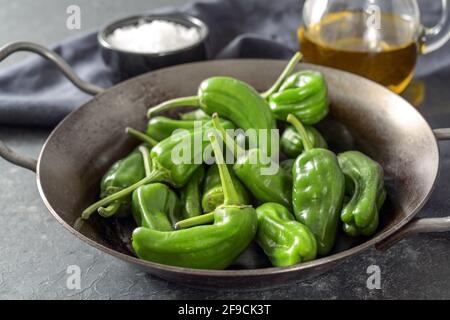 Frische grüne Pimientos oder Paprika de padron in einer Eisentopf-Pfanne. In Olivenöl gebraten und mit Meersalz bestreut ist eine typische Tapa-Mahlzeit in Spanien. Dunkelgrau Stockfoto