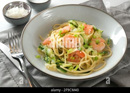 Nudelgericht aus Spaghetti, Zucchini, Frühlingszwiebeln und Garnelen in einem grauen Teller auf einer Serviette mit Parmesan Schüssel und Besteck, mediterrane Küche, selec Stockfoto