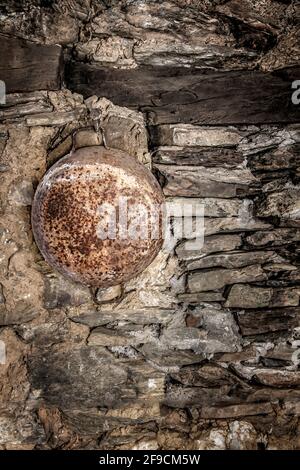 Alter, rostiger Kessel, der an einer alten Steinmauer eines ländlichen Hauses senkrecht hängt Stockfoto