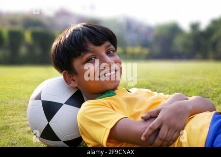 Kleiner Junge, der mit Fußball auf dem Boden liegt Stockfoto