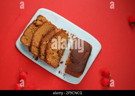 Pflaumenkuchen, hausgemachter leckerer Christmus-Kuchen mit Rosinen, Cashewnüssen und getrockneten Früchten, die in Scheiben geschnitten und mit rotem Backgro an Bord platziert werden Stockfoto