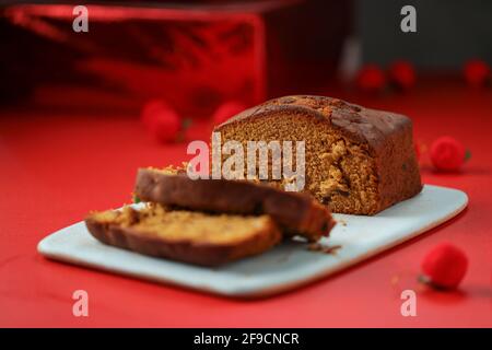 Pflaumenkuchen, hausgemachter leckerer Christmus-Kuchen mit Rosinen, Cashewnüssen und getrockneten Früchten, die in Scheiben geschnitten und mit rotem Backgro an Bord platziert werden Stockfoto