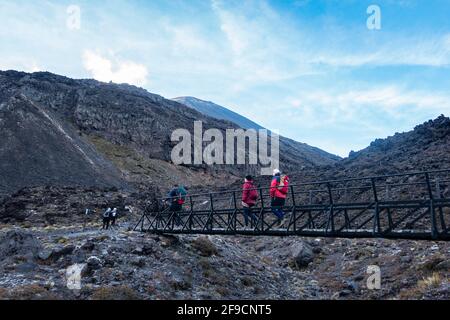 Tongariro Neuseeland - 27 2021. März; Tramper überqueren im Morgenlicht eine kleine Brücke, eingerahmt von vulkanischer Landschaft auf einem der Great Walks Neuseelands Stockfoto