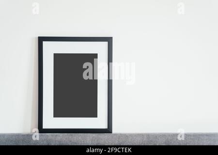 Im Innenraum steht ein leerer Bilderrahmen aus Holz auf weißem Hintergrund. Mockup-Posterrahmen. Stockfoto
