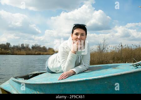 Eine Frau mittleren Alters genießt die frische Luft im frühen Frühjahr auf dem Fluss. Die Frau trägt einen weißen Sportpullover. Stockfoto