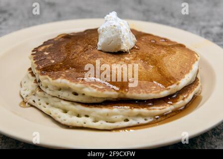 Kurzer Stapel Pfannkuchen, tropfend mit Ahornsirup und gekrönt mit Schlagbutter. Stockfoto