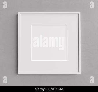 Leerer weißer Bilderrahmen mit quadratischer Form an einer grauen Wand. Leeres Mockup für Bilder und Fotos. Stockfoto
