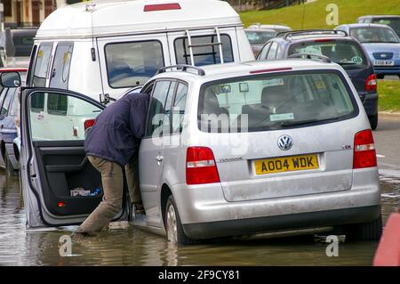 Flutung in Southend am Meer. Der Mensch wasiert durch Tiefseewasser zu seinem Auto. Die Frühjahrsflut brach gegen die Verteidigung des Meeres. Nasse Füße Stockfoto