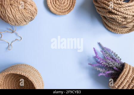 Der gestrickte Teil des Korbes aus Jute-Seil und der Häkelhaken auf blauem Hintergrund, freier Platz. Hobbys, Handarbeiten, Organisation des Raumes. Stockfoto