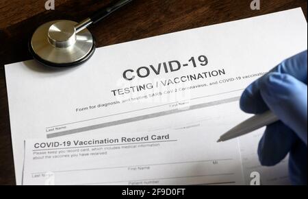 COVID-19 Test- und Impfformulare am Schreibtisch, Arzt nimmt einen Eintrag in Coronavirus-Impfpass, medizinisches Dokument in der Klinik. Konzept von coron Stockfoto