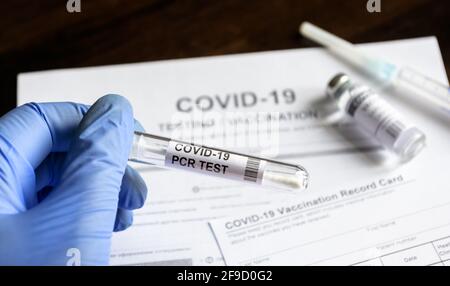 COVID-19 PCR-Test in ärztlicher Hand in der Klinik, Coronavirus-Abstrichbesteck auf medizinischen Formen und Impfstoffhintergrund. Konzept des Corona-Virus-Tests, Stockfoto