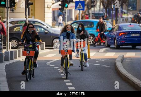 Bukarest, Rumänien - 01. April 2021: Drei junge Frauen fahren auf dem Fahrradweg der Victory Avenue mit gemieteten Fahrrädern. Dieses Bild ist nur für redaktionelle Zwecke bestimmt. Stockfoto