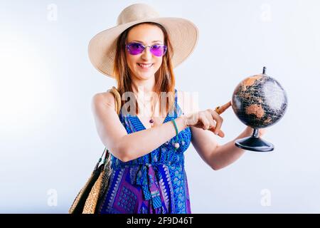 Lächelnd schöne junge Frau im Sommer Strandkleid mit einem terrestrischen Globus zeigt mit dem Finger. Reiseziel Konzept auf weißem Hintergrund Stockfoto